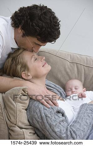 Stock Photo - Mid adult woman holding her baby while being kissed by a mid adult man. Fotosearch