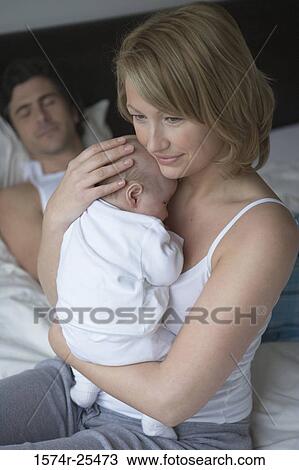 Mid adult woman holding her baby with a mid adult man sleeping in the background View Large Photo Image Stock Image - Mid adult woman holding her baby with a mid adult man sleeping in the background. Fotosearch