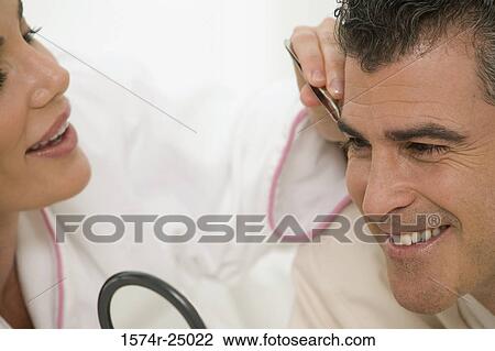 Stock Image - Mid adult woman plucking the eyebrows of a mature man. Fotosearch