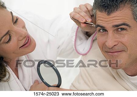 Stock Image - Mid adult woman plucking the eyebrows of a mature man. Fotosearch