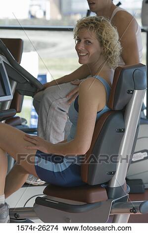 Picture - Mid adult woman sitting on a stationary recumbent bicycle. Fotosearch