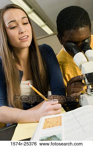 One student looking through a microscope with another student writing View Large Photo Image Stock Photograph - One student looking through a microscope with another student writing. Fotosearch
