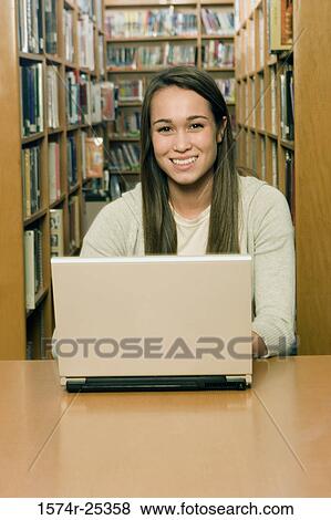 Portait of a student sitting in front of a laptop in a library View Large Photo Image Stock Photo - Portait of a student sitting in front of a laptop in a library. Fotosearch