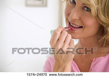 Stock Image - Portrait of a mid adult woman applying lipstick to her lips. Fotosearch