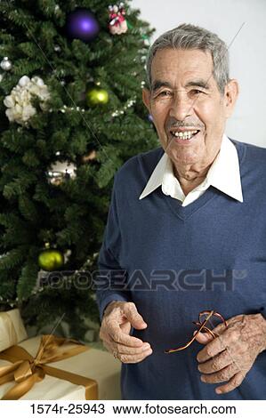 Portrait of a senior man standing near a Christmas tree and smiling View Large Photo Image Stock Image - Portrait of a senior man standing near a Christmas tree and smiling. Fotosearch