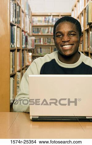 Picture - Portrait of a student sitting in front of a laptop in a library. Fotosearch