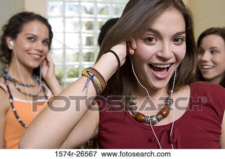 Stock Photo - Portrait of a teenage girl listening to music with her friends in the background. Fotosearch