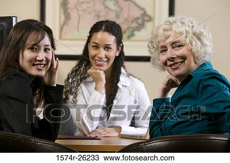 Stock Image - Portrait of three businesswomen sitting at a desk. Fotosearch