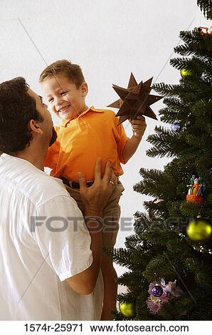 Rear view of a mature man holding his son and standing near a Christmas tree View Large Photo Image Stock Image - Rear view of a mature man holding his son and standing near a Christmas tree. Fotosearch