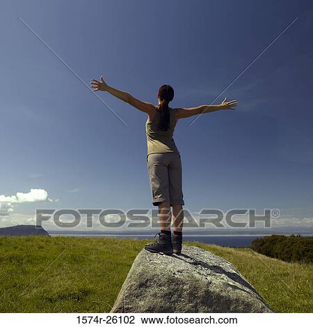 Rear view of a mid adult woman standing on a rock with her arms outstretched View Large Photo Image Stock Image - Rear view of a mid adult woman standing on a rock with her arms outstretched. Fotosearch