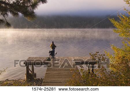 Stock Image - Rear view of a person fishing on a pier. Fotosearch