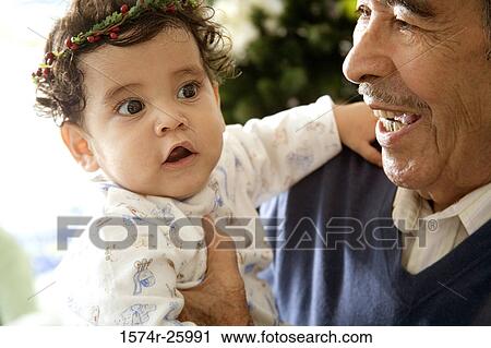 Stock Image - Senior man holding his great-grandchild and smiling. Fotosearch