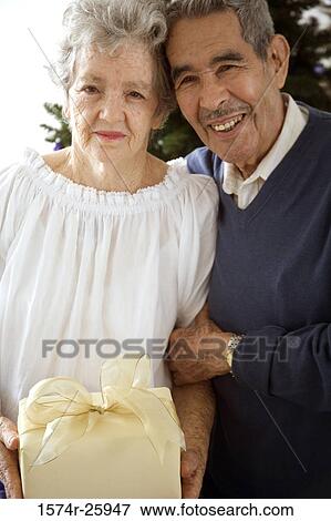 Senior woman holding a gift with a senior man standing beside her View Large Photo Image Stock Photo - Senior woman holding a gift with a senior man standing beside her. Fotosearch