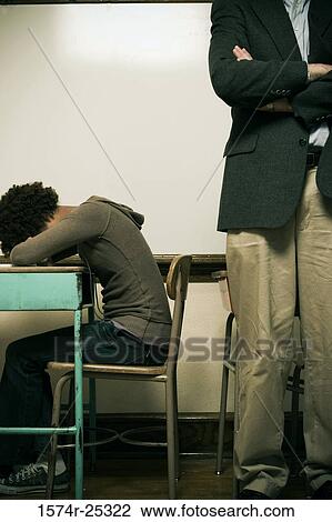 Stock Image - Teacher standing next to a student sleeping at her desk. Fotosearch