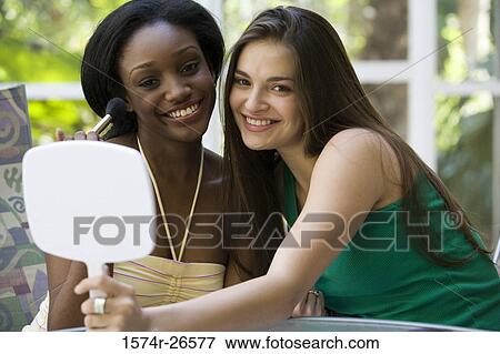 Teenage girl holding a mirror for a young woman applying make-up View Large Photo Image Stock Photo - Teenage girl holding a mirror for a young woman applying make-up. Fotosearch