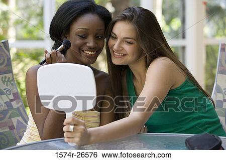 Stock Photograph - Teenage girl holding a mirror for a young woman applying make-up. Fotosearch