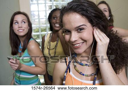 Picture - Teenage girl listening to music with her friends in the background. Fotosearch
