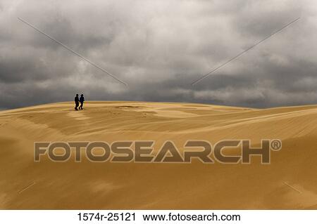 Stock Image - Two people walking on sand in a desert. Fotosearch