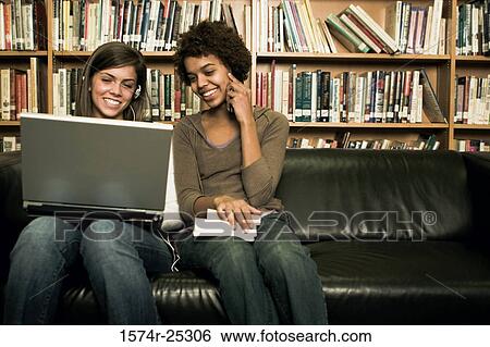 Stock Photograph - Two students sitting on a couch in a library with a laptop. Fotosearch