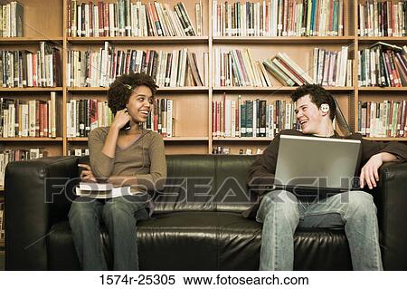 Two students sitting on a couch in a library View Large Photo Image Stock Photography - Two students sitting on a couch in a library. Fotosearch