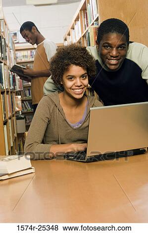 Stock Photo - Two students using a laptop with another student in the background. Fotosearch