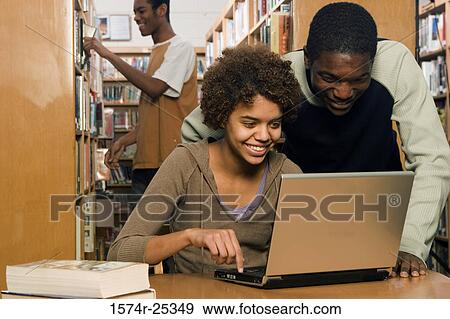 Two students using a laptop with another student in the background View Large Photo Image Stock Photo - Two students using a laptop with another student in the background. Fotosearch