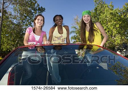 Two teenage girls and a young woman standing in a convertible car View Large Photo Image Picture - Two teenage girls and a young woman standing in a convertible car. Fotosearch