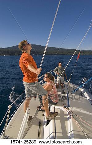 Stock Photo - Two young men and a young woman on a sailboat. Fotosearch