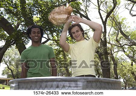 Two young men throwing trash in a garbage can View Large Photo Image Stock Image - Two young men throwing trash in a garbage can. Fotosearch