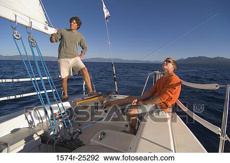 Young man pulling a rope on a sailboat with another young man standing beside him View Large Photo Image Stock Image - Young man pulling a rope on a sailboat with another young man standing beside him. Fotosearch