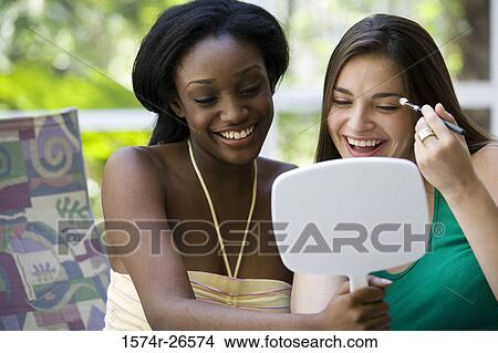 Young woman holding a mirror for a teenage girl applying make-up View Large Photo Image Picture - Young woman holding a mirror for a teenage girl applying make-up. Fotosearch