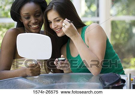 Stock Photography - Young woman holding a mirror for a teenage girl applying make-up. Fotosearch
