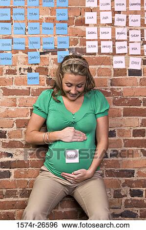 Young woman looking at an adhesive note with baby name stuck on her abdomen View Large Photo Image Stock Photograph - Young woman looking at an adhesive note with baby name stuck on her abdomen. Fotosearch