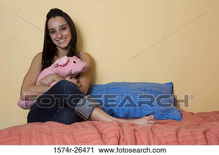 Stock Image - Young woman sitting on a bed and holding a stuffed animal. Fotosearch