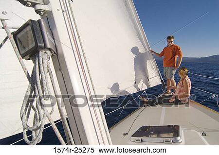 Young woman sitting on a sailboat with a young man standing beside her View Large Photo Image Stock Photography - Young woman sitting on a sailboat with a young man standing beside her. Fotosearch