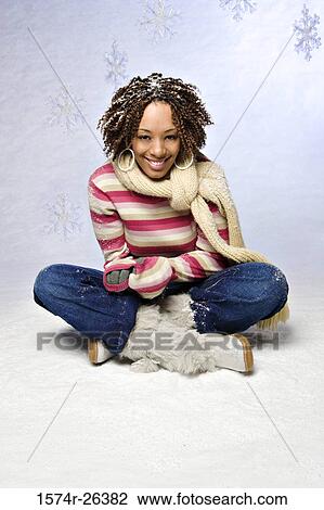 Stock Image - Young woman sitting on snow and smiling. Fotosearch