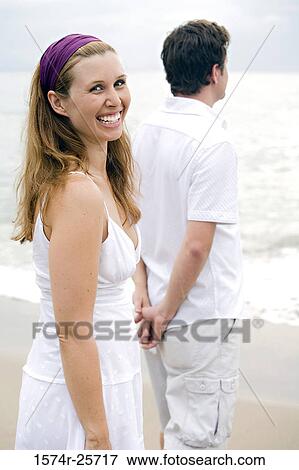 Young woman smiling with a mid adult man standing beside her on the beach View Large Photo Image Stock Photo - Young woman smiling with a mid adult man standing beside her on the beach. Fotosearch