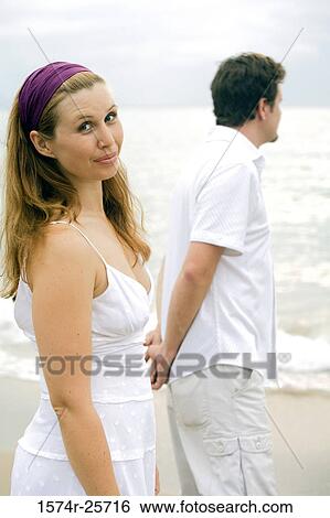Young woman smirking with a mid adult man standing beside her on the beach View Large Photo Image Stock Photograph - Young woman smirking with a mid adult man standing beside her on the beach. Fotosearch