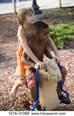 Stock Photo - Bare chested boys sitting on spring horse. Fotosearch