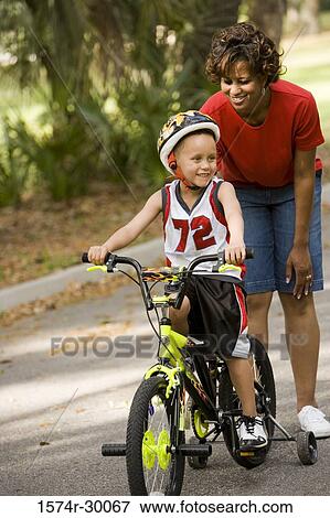 Boy cycling a bicycle while mother standing behind him on the road View Large Photo Image Stock Photo - Boy cycling a bicycle while mother standing behind him on the road. Fotosearch