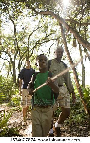 Boy holding a stick while others walking behind him at forest View Large Photo Image Picture - Boy holding a stick while others walking behind him at forest. Fotosearch