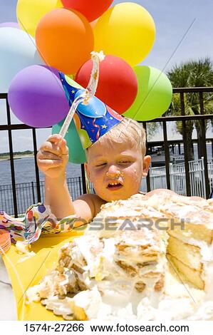 Boy holding balloons in front of a birthday cake View Large Photo Image Stock Photograph - Boy holding balloons in front of a birthday cake. Fotosearch
