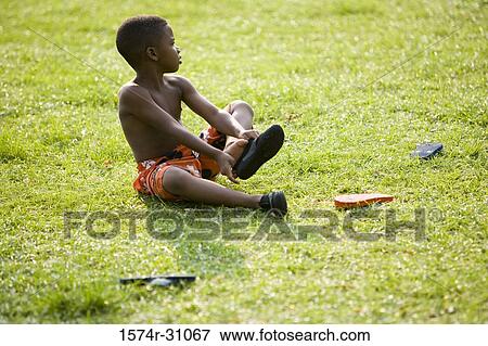Stock Photo - Boy sitting on grass and removing flip-flops. Fotosearch