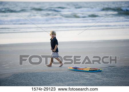 Boy walking with surfboard at the beach View Large Photo Image Stock Image - Boy walking with surfboard at the beach. Fotosearch