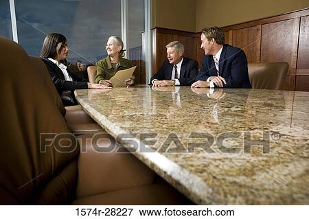 Business people sitting by conference table and discussing in an office View Large Photo Image Stock Photo - Business people sitting by conference table and discussing in an office. Fotosearch