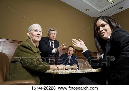Stock Photo - Business people sitting by conference table and discussing in an office. Fotosearch