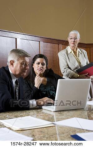 Business people sitting by conference table and using laptop in an office View Large Photo Image Stock Photo - Business people sitting by conference table and using laptop in an office. Fotosearch
