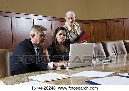 Stock Photo - Business people sitting by conference table and using laptop in an office. Fotosearch