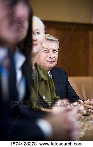 Stock Photo - Business people sitting by conference table in an office. Fotosearch