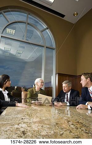 Business people sitting by conference table and discussing in an office View Large Photo Image Stock Photograph - Business people sitting by conference table and discussing in an office. Fotosearch